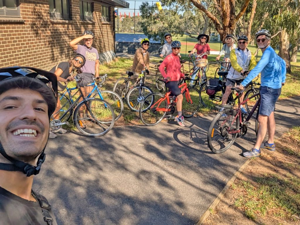 Group of cyclists gathered outdoors, Neighbourly Ride, smiling and posing for a photo before a ride.