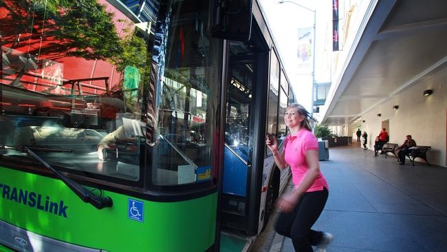 A woman in a pink top jogs toward the open door of a green TransLink bus